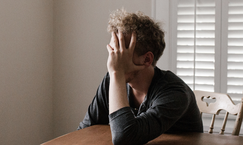Man leaning on a table, hiding his face and head in his hands